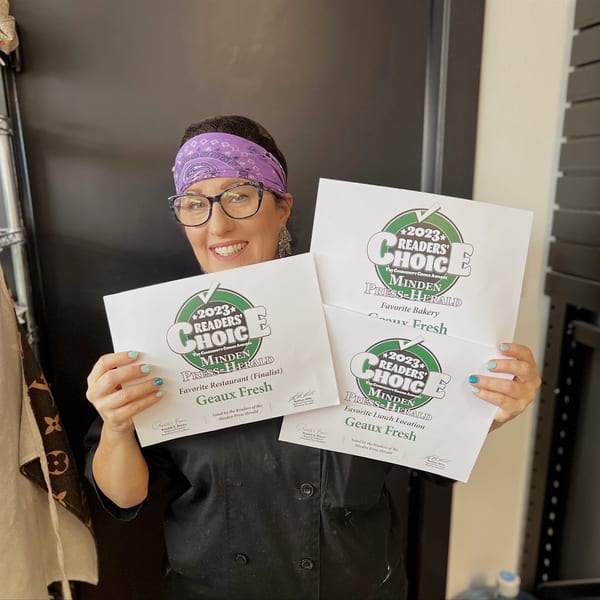 A smiling woman in a purple bandana and glasses holds up three "2023 Readers' Choice" awards for Geaux Fresh.